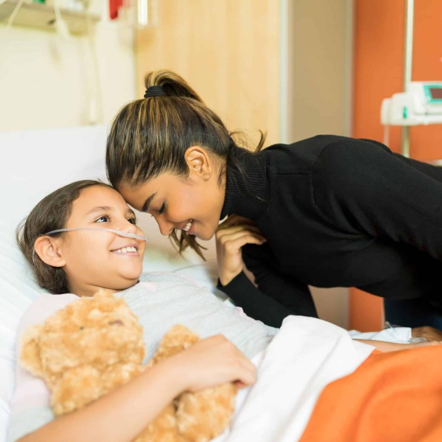 smiling-mother-unwell-daughter-by-bed-hospital-visit-min-min smiling-mother-unwell-daughter-by-bed-hospital-visit-min-min